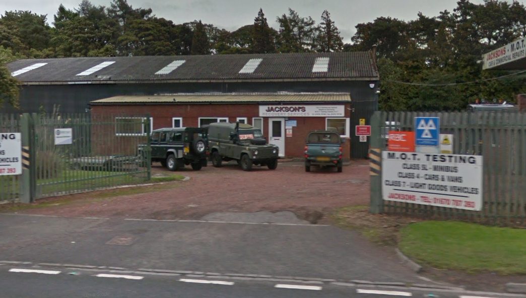 The garage at Priestbridge from the road, with the JACKSONS sign and the M.O.T. testing board